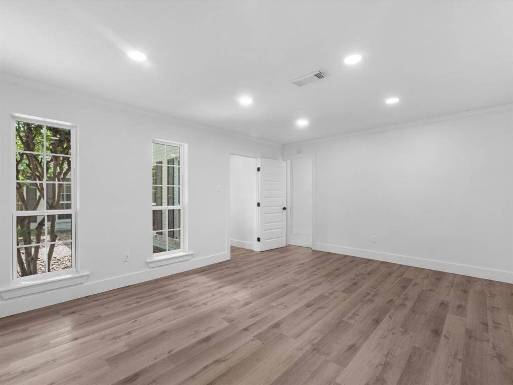 This room features bright, open space with light wood flooring and recessed lighting. Large windows allow for natural light, and a white door provides access to another area. Perfect for customization and versatile use.
