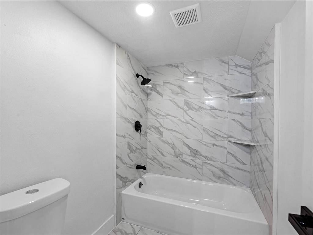 This bathroom features a sleek design with white marble-look tile surrounding a bathtub and shower area. It has modern black fixtures and a simple, clean aesthetic, perfect for a contemporary home.