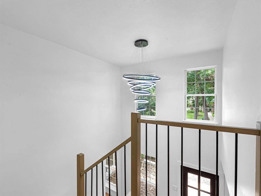 This photo showcases a bright, airy stairwell with a modern spiral chandelier. Large windows provide natural light and views of greenery. The design features a sleek railing and a welcoming entrance below.