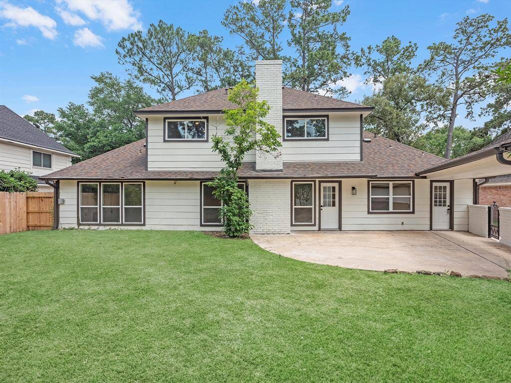 This photo showcases a charming two-story home with a spacious backyard and a large patio area. The exterior features a mix of siding and brick, with a central chimney. Surrounded by mature trees, it offers both privacy and a natural setting.
