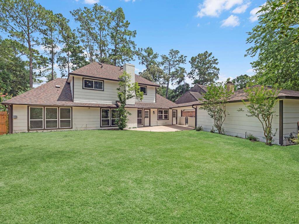 This photo shows a spacious backyard with a well-maintained lawn and a two-story house featuring a mix of light-colored siding and windows. The property is surrounded by mature trees, offering privacy and a natural setting.