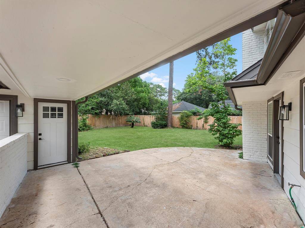 This photo showcases a covered patio area leading to a spacious, fenced backyard with lush greenery, perfect for outdoor activities and relaxation.