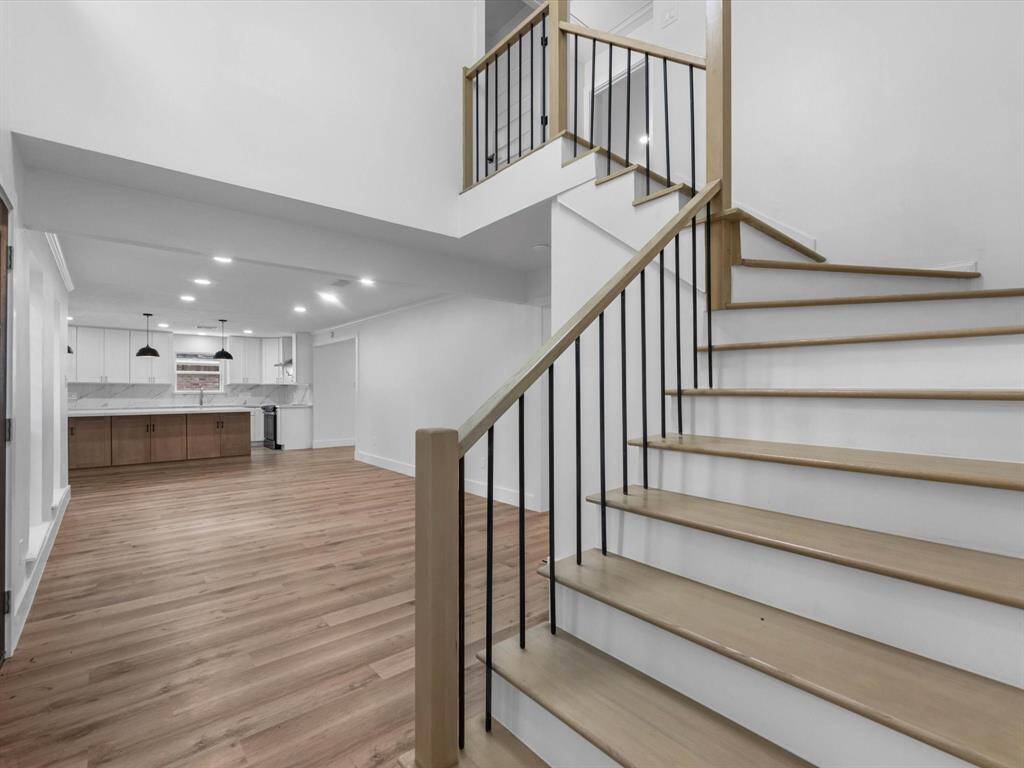 This photo showcases a modern, open-concept living space with sleek wooden flooring and a stylish staircase. The kitchen features elegant white cabinetry, marble countertops, and pendant lighting, creating a bright and inviting atmosphere.