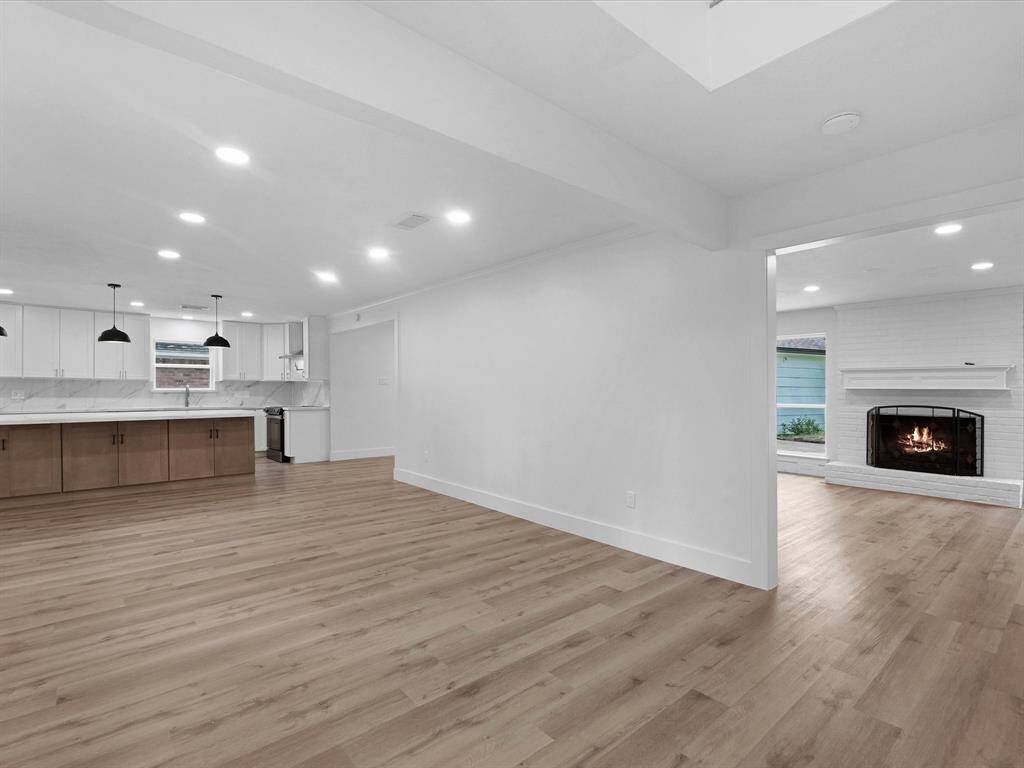 This spacious open-concept area features a modern kitchen with marble countertops, a large island, and pendant lighting. Adjacent is a cozy living room with a fireplace and wood flooring, creating a warm, inviting atmosphere.