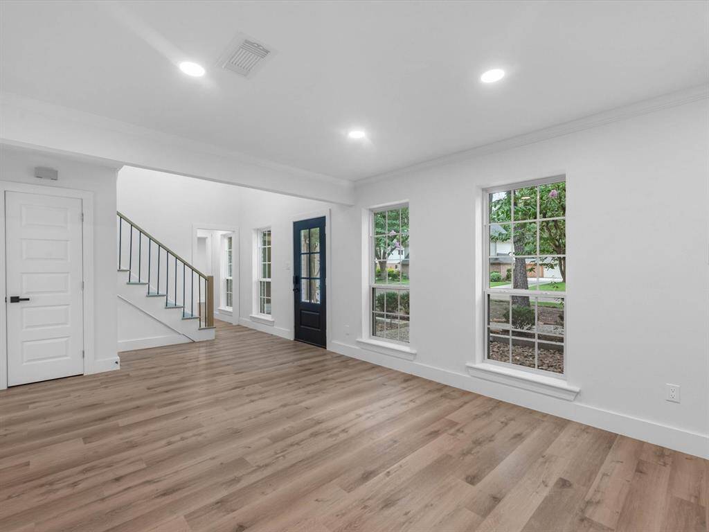 Bright and airy living space with large windows, wood flooring, and a modern staircase. The open layout and neutral colors create an inviting atmosphere.