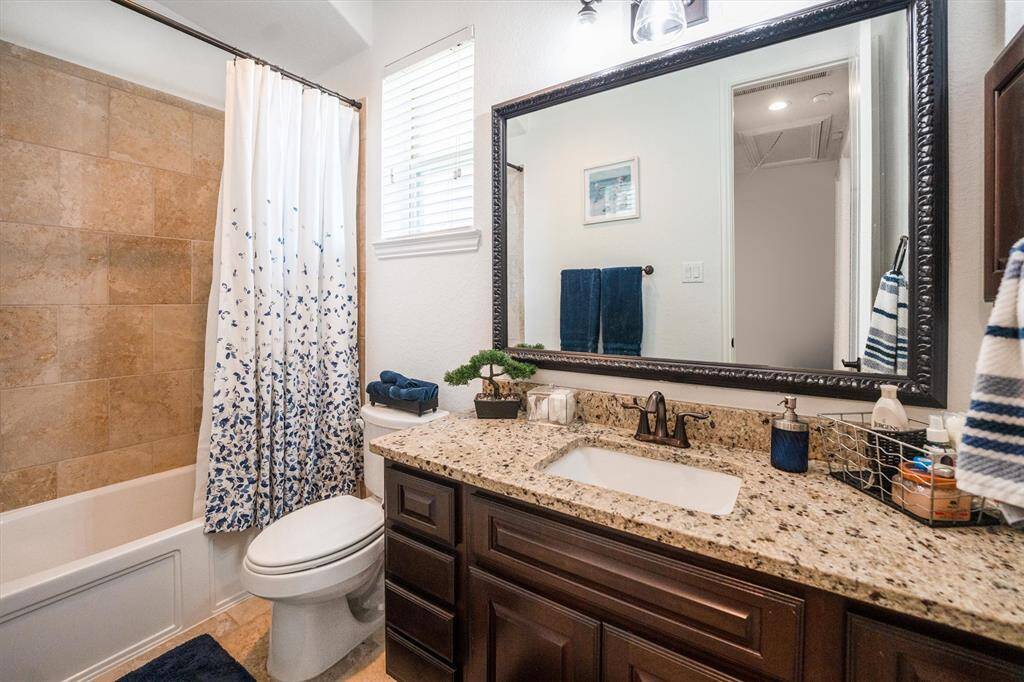 Elegant bathroom featuring a tub/shower combo, framed mirror, and luxurious granite countertops.
