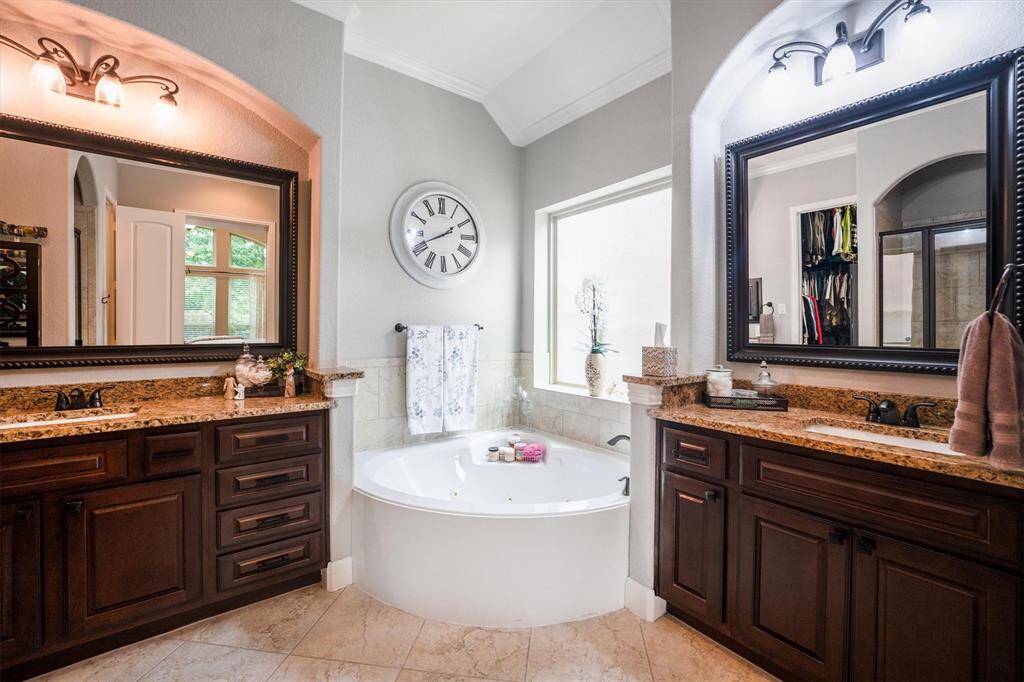 Luxurious bathroom with granite vanities, elegant framed mirrors, a soothing whirlpool tub, separate shower, and refined crown molding.