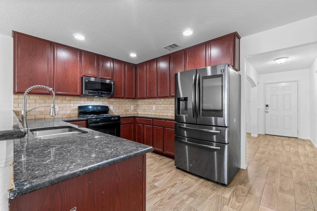 This modern kitchen features sleek stainless steel appliances, rich 42 inch wooden cabinetry, and granite countertops. The space is illuminated with recessed lighting and has a stylish tiled backsplash.