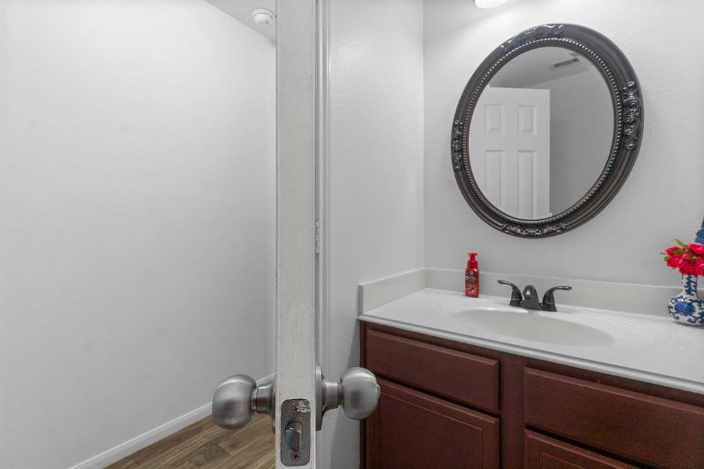 This photo shows a small, stylish bathroom with a vanity featuring dark wood cabinets and a white countertop. The room has clean white walls and wood-look flooring, creating a fresh and inviting atmosphere.