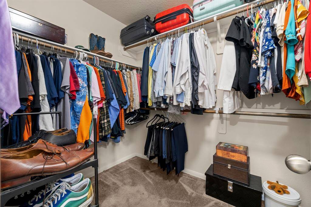 A spacious walk-in closet in this owners retreat with ample hanging space for clothes, shelves for shoes, and luggage storage on top.