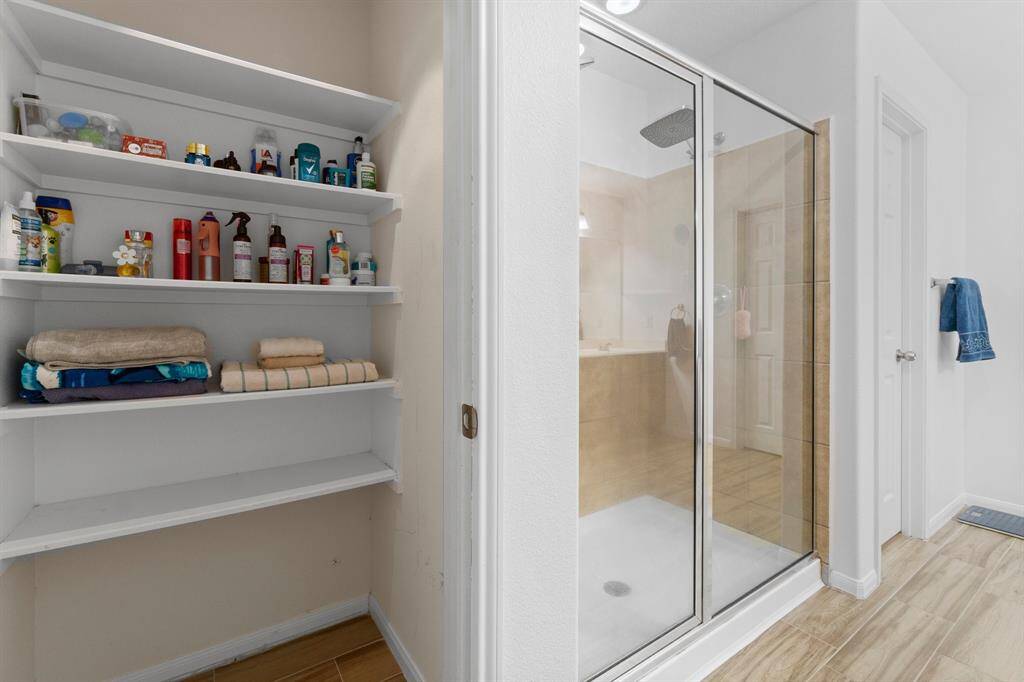 This bathroom features a spacious glass-enclosed shower and convenient built-in shelving for storage. The room has a clean, modern look with light-colored tiles and walls.