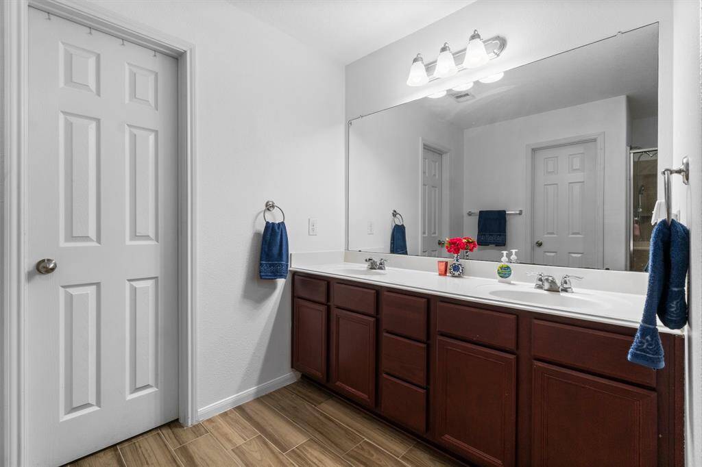 This bathroom features a double sink vanity with dark wood cabinets, a large mirror, and modern lighting. It has a clean, bright look with fresh white walls and wood-style flooring.