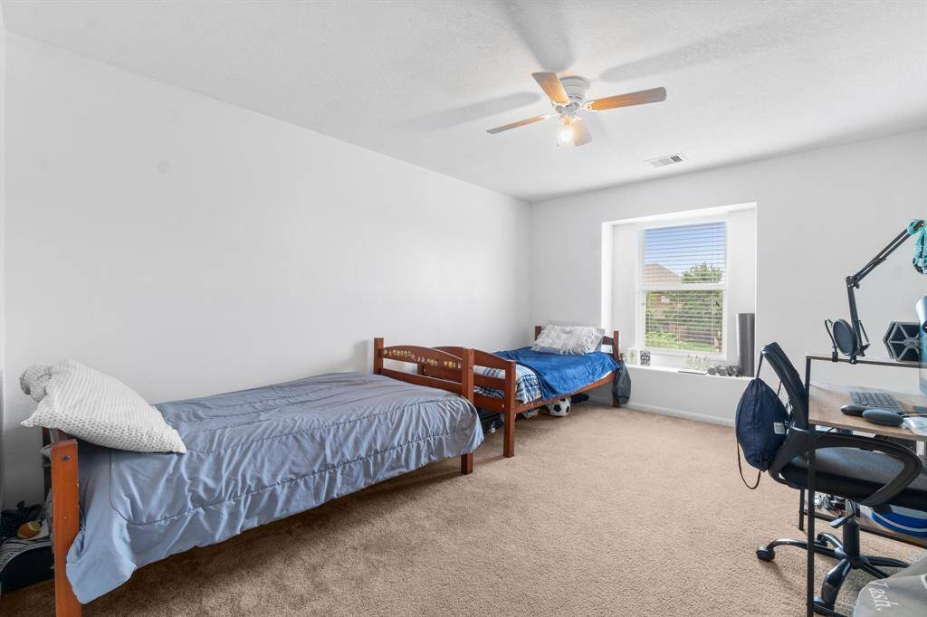 This room is bright and spacious, featuring two single beds and a window that lets in natural light. It has a neutral carpet, a ceiling fan, and a desk setup, ideal for a child's or guest bedroom. With a large walkin closet this room can comforably host two.
