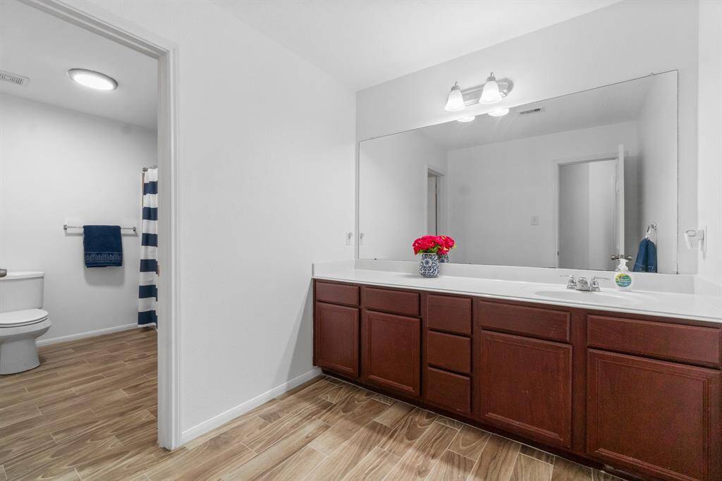 This bathroom features a spacious layout with wood-look tile flooring, a large vanity, and ample cabinetry. It includes a separate area with a toilet and shower.