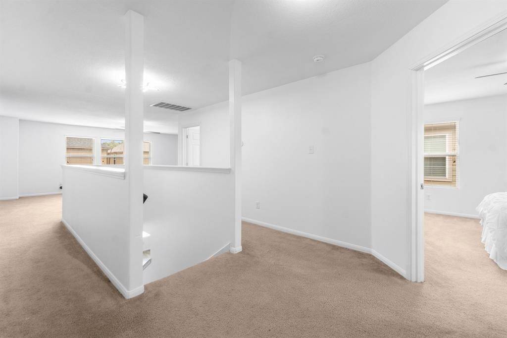 This photo shows a bright and spacious upstairs landing area with neutral carpeting and white walls. It features an open layout with access secondary bedrooms, game room and media room allowing plenty of natural light from multiple windows.