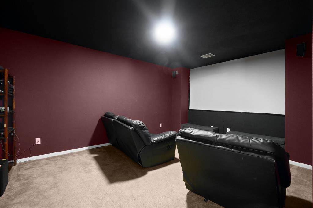 Cozy home theater with plush black sofas, dark red walls, a large screen, and surround sound setup, perfect for movie nights!