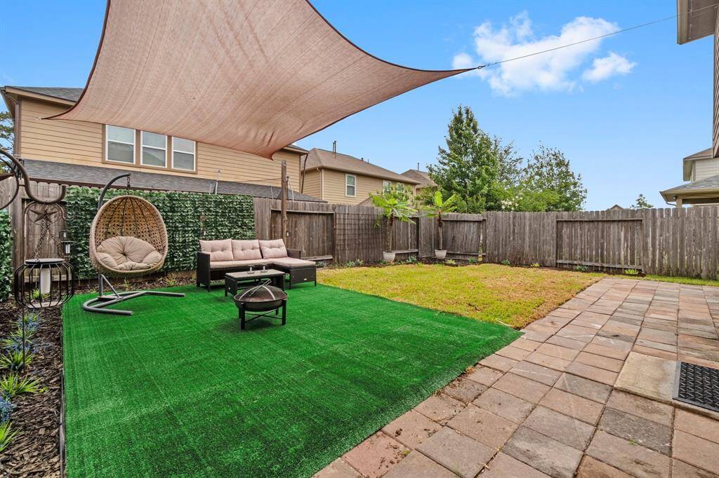 Charming backyard with a mix of artificial turf and pavers, featuring cozy outdoor seating under a shade sail. The space is enclosed by a wooden fence, providing privacy and a welcoming atmosphere for relaxation or entertaining.