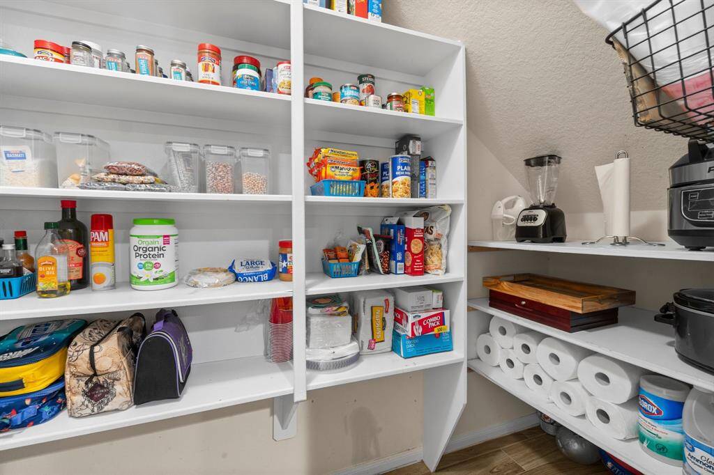 This photo showcases a well-organized pantry with white shelves stocked with various food items, containers, and kitchen appliances. The space includes ample storage for groceries and household supplies.  Small appliances are neatly placed on the side, indicating a functional and efficient layout.