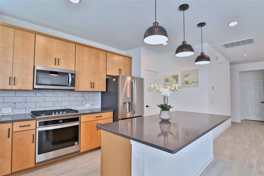 This modern kitchen features sleek wood cabinetry, stainless steel appliances, and a large island with pendant lighting. The backsplash adds a touch of elegance, and the open layout enhances space and functionality.