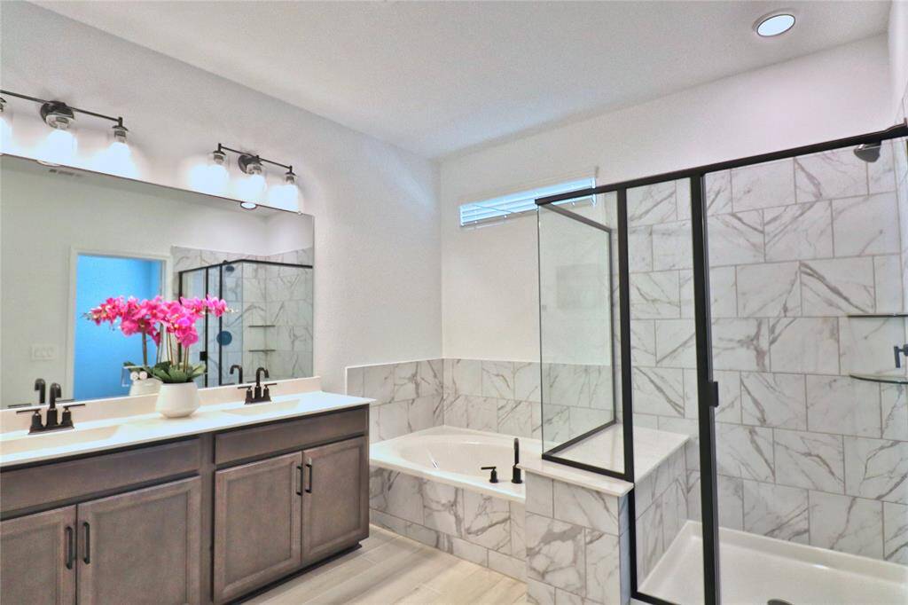 The primary bathroom features a double vanity with elegant lighting, a spacious glass-enclosed shower, and a luxurious soaking tub. The neutral tones and marble accents create a serene, spa-like atmosphere.