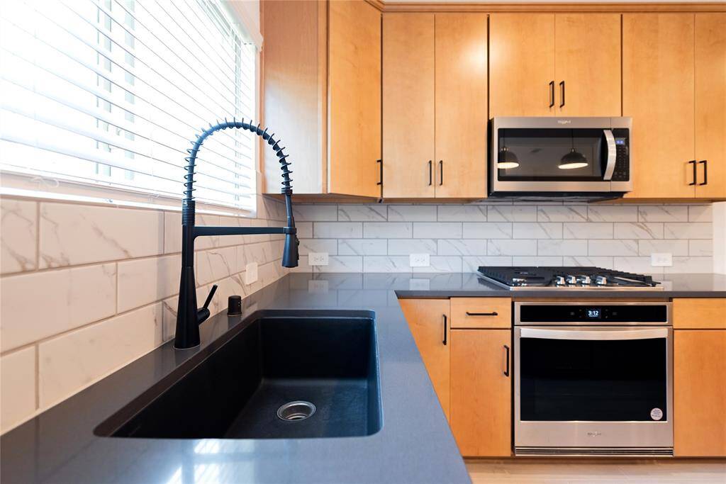 Modern kitchen with sleek black fixtures, stainless steel appliances, and light wood cabinetry. The space features a stylish backsplash and a large window providing ample natural light.