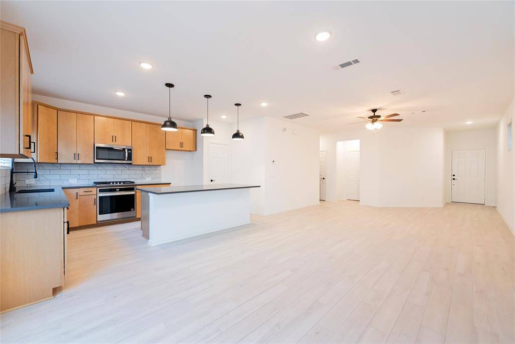 It features a spacious open-concept kitchen and living area with  wood like tile flooring. The space is well-lit with recessed lighting and a ceiling fan in the living area.