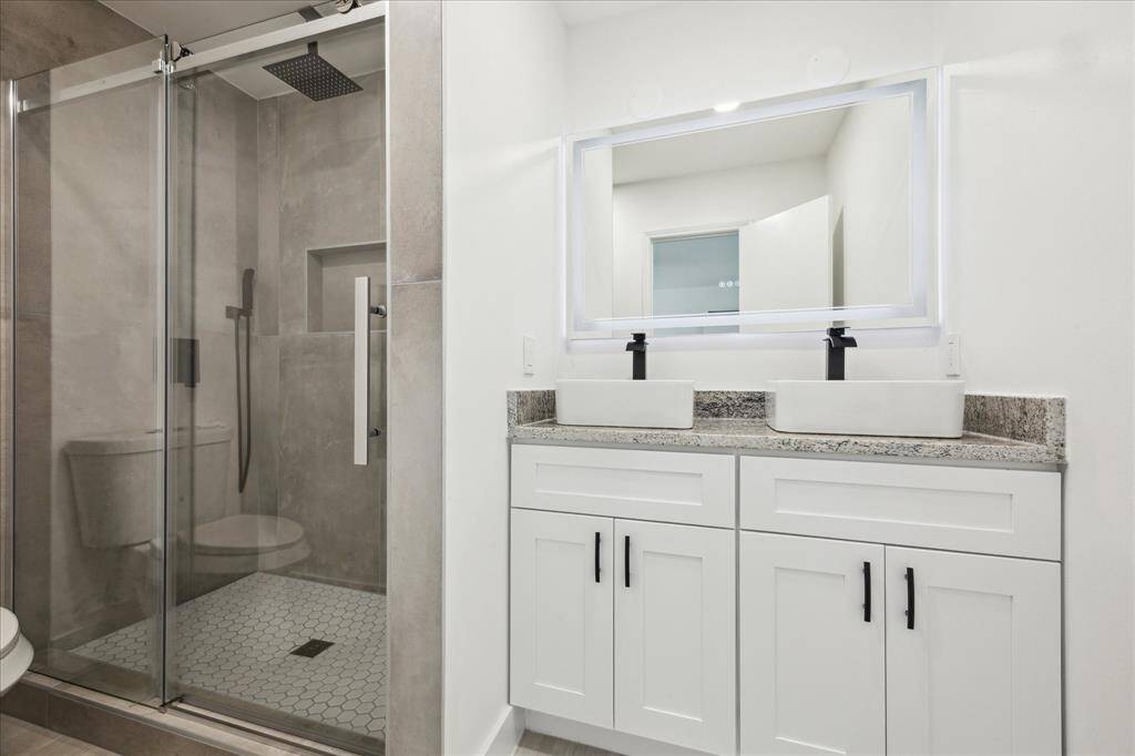 The primary bath features a rainfall shower head with wand, frameless glass shower, double sinks, and striking black and white granite countertops