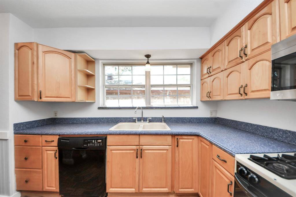 A spacious kitchen equipped with a Whirlpool dishwasher, gas stove, and a stainless steel LG microwave. A large window fills the space with natural light, while abundant cabinets, drawers, and a pantry provide plenty of storage.
