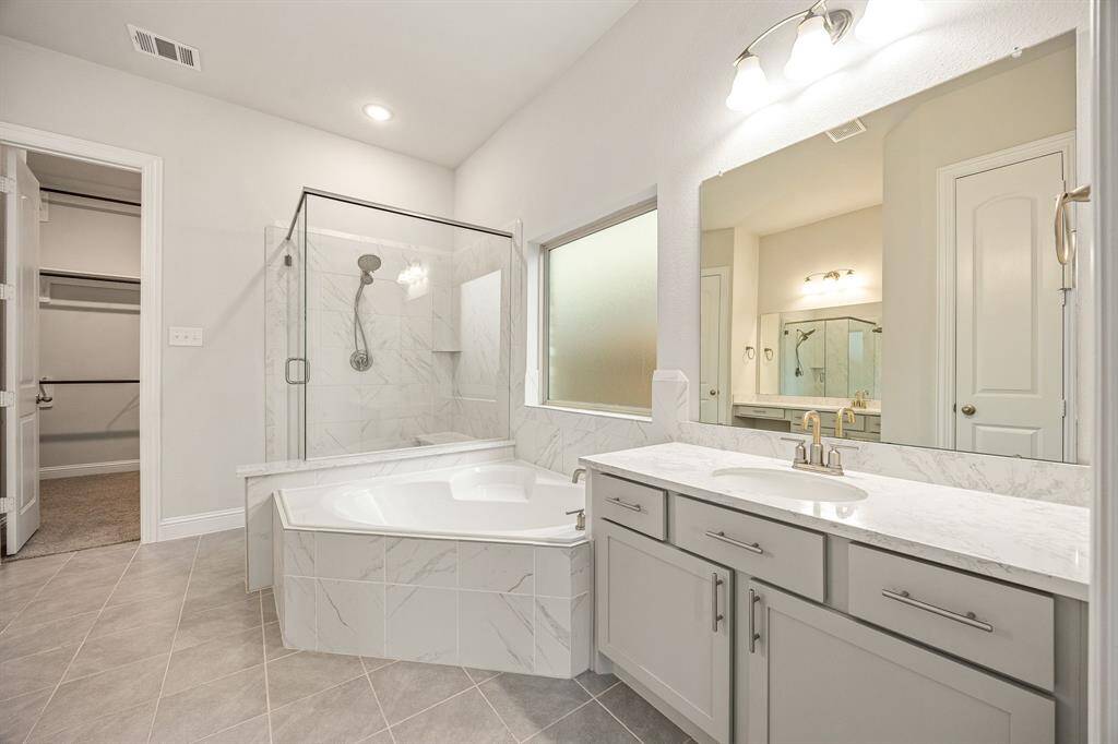 Step into a spa-inspired oasis in this move-in ready primary bathroom. Indulge in the oversized walk-in shower with elegant tile surround or unwind in the luxurious garden tub, complete with custom tile accents. Sleek gray cabinetry is topped with beautiful granite countertops, adding a modern touch to this serene space. High ceilings, custom paint, and sophisticated finishes enhance the upscale feel, while a spacious walk-in closet with built-in shelving offers both convenience and style.