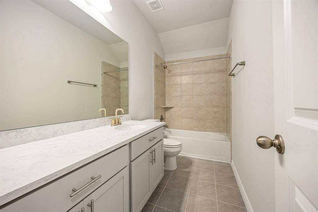 A spacious shower/tub combo with a beautifully tiled surround adds a touch of luxury, while the large mirror and neutral paint create a bright, inviting atmosphere. With durable tile flooring and thoughtful finishes, this bathroom is perfectly equipped to comfortably accommodate visiting family or guests.