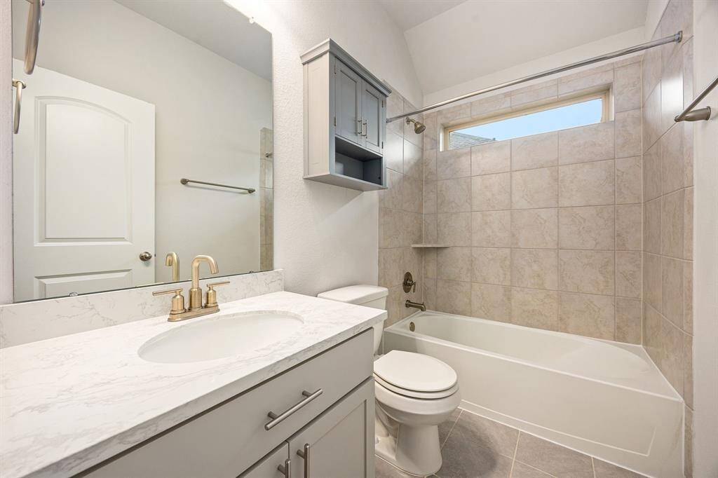 A generously sized shower/tub combo with stylish tile surround brings a refined, upscale feel to the space. The expansive mirror and soft, neutral tones enhance the sense of light and openness. Finished with durable tile flooring and contemporary accents, this bathroom offers both comfort and convenience—ideal for hosting overnight guests or extended family visits.