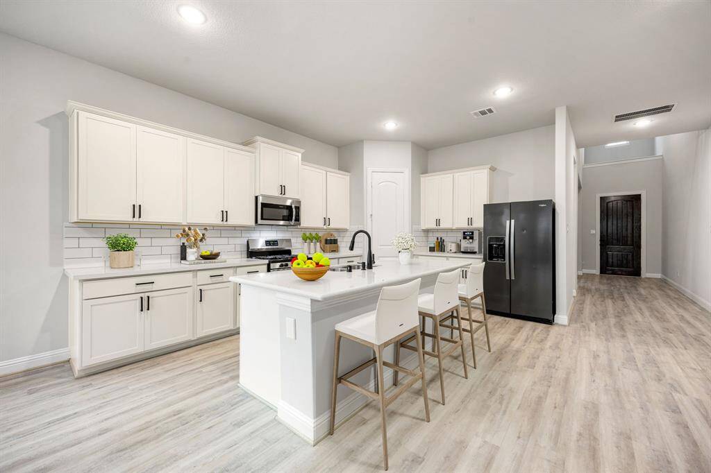 Take a moment to admire this pristine, show-stopping kitchen—where functionality meets elegant design. Thoughtfully connected to the breakfast nook, dining area, and living room, this layout makes hosting and everyday living feel effortless. Light-toned cabinetry brightens the space, while rich wood flooring adds warmth and character. An expansive island with a built-in breakfast bar invites casual dining and conversation, and the walk-in pantry, along with generous counter space, ensures you’re always prep