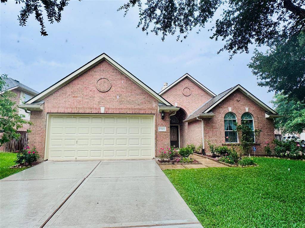 This charming brick home features a well-maintained front yard with lush greenery and a clean, wide driveway leading to a two-car garage. The arched windows and entryway add a touch of elegance, while mature trees provide shade and character.