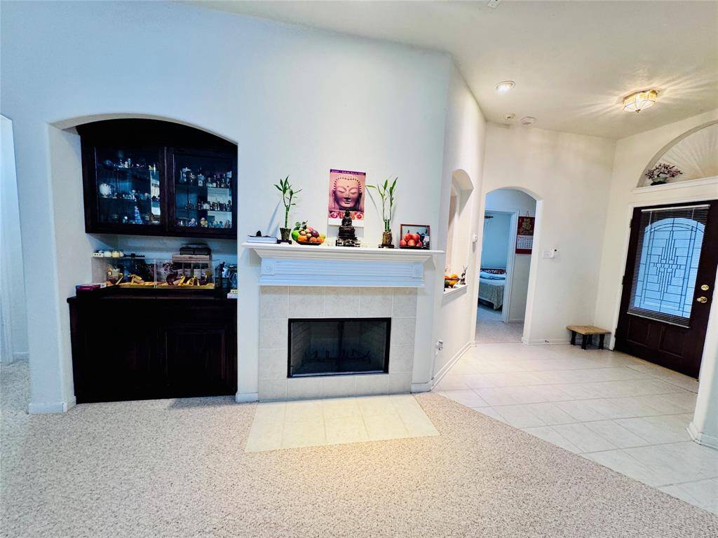 This inviting living space features a cozy fireplace, built-in display cabinet, and a mix of carpet and tile flooring. The entryway is highlighted by a decorative glass door, while arched doorways add charm and character.