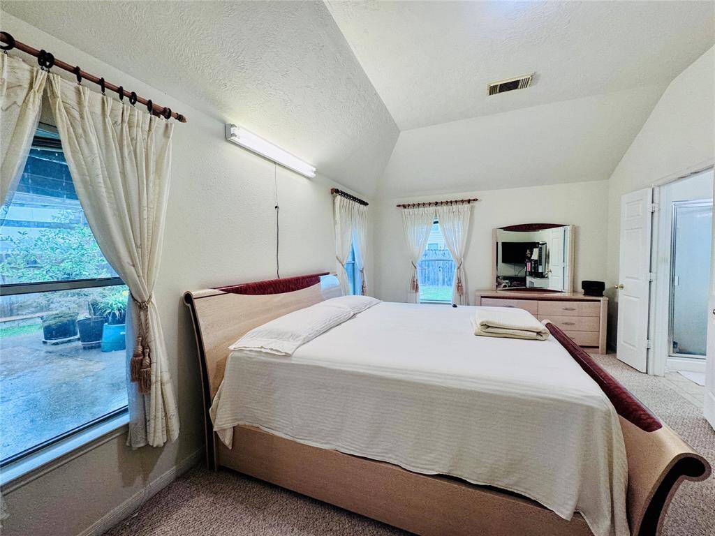Spacious bedroom with high ceilings, multiple windows offering natural light and views of the garden.
