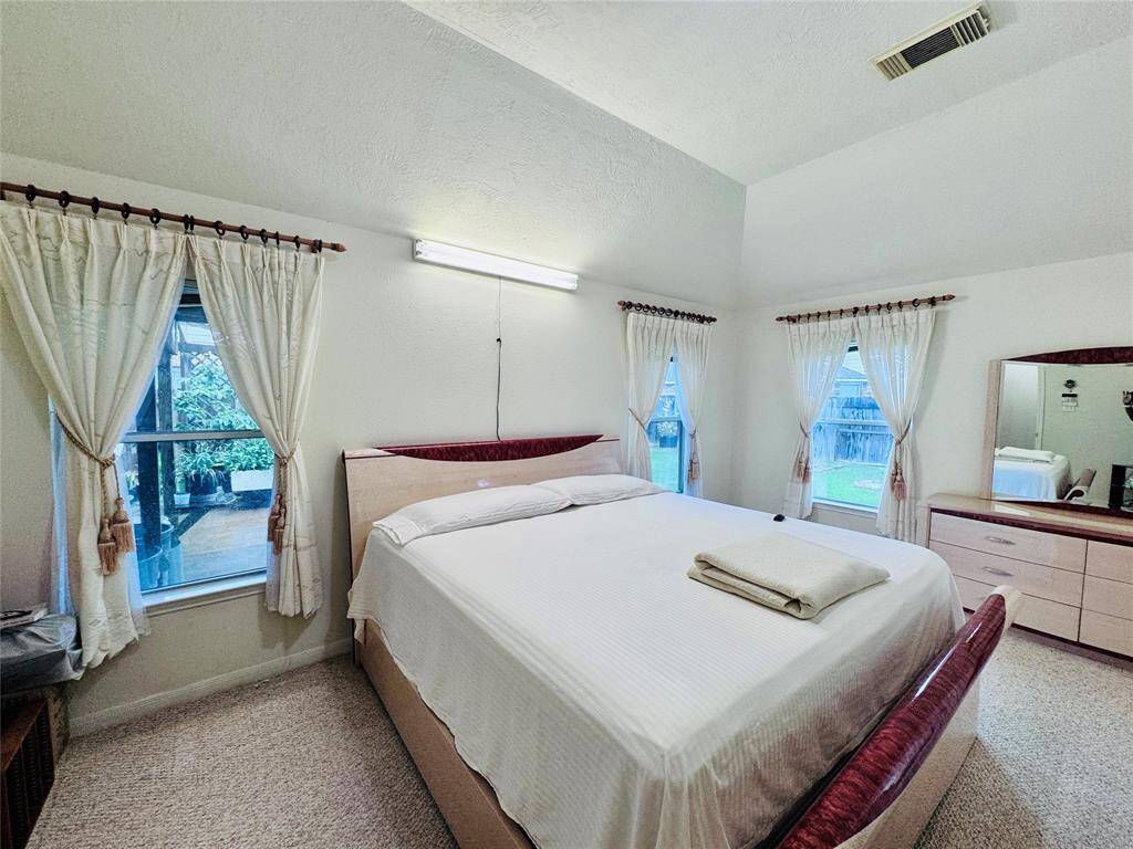 Spacious bedroom with high ceilings, multiple windows offering natural light and views of the garden.