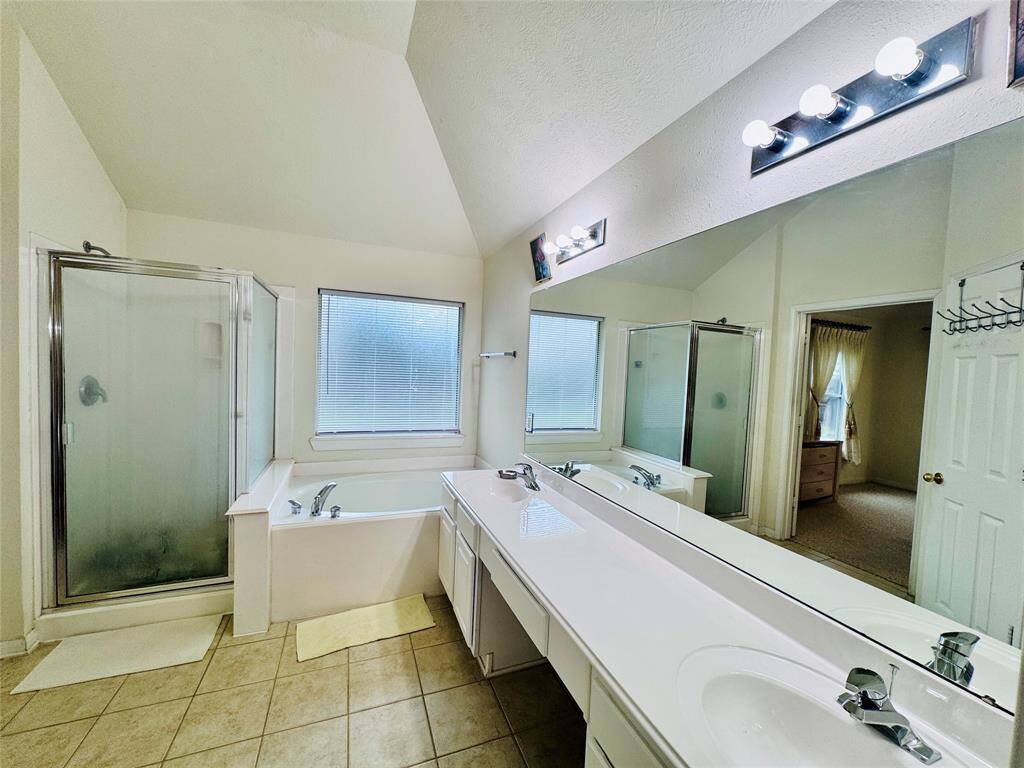 This spacious Primary bathroom features dual sinks with a long vanity, a separate glass-enclosed shower, and a soaking tub. It has ample natural light from a large window