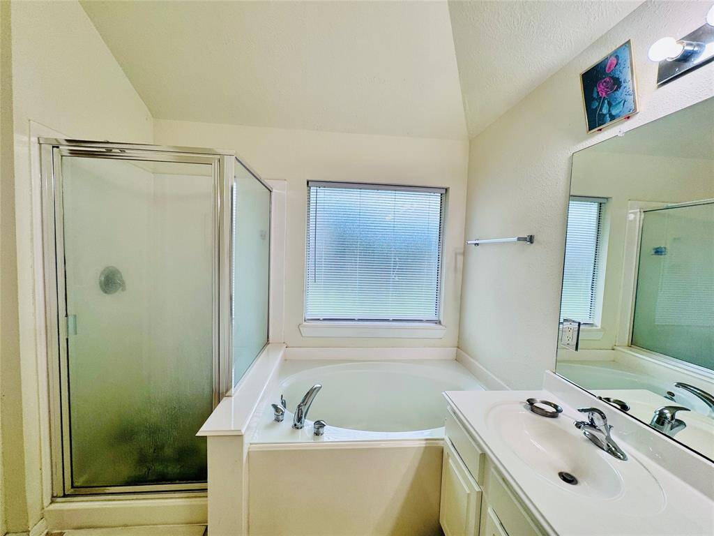 Bright bathroom featuring a spacious corner bathtub, separate glass-enclosed shower, and a single-sink vanity with ample counter space. A large window provides natural light.