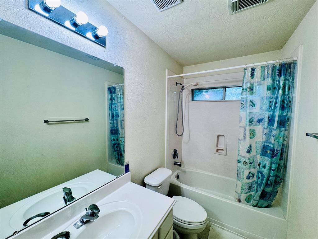 This bathroom features a clean design with a white vanity, a mirror with bright lighting, a bathtub with a shower, and a window for natural light.