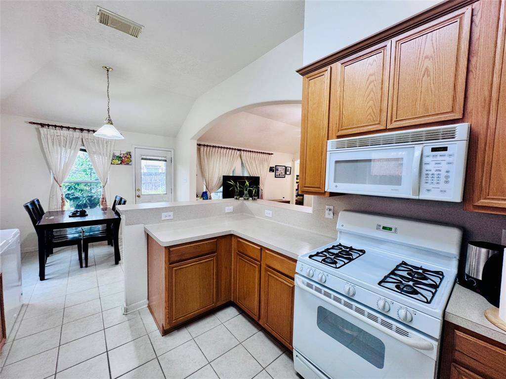 Bright kitchen with wooden cabinets, gas stove, and microwave. Open layout connects to dining area with natural light and outdoor access.