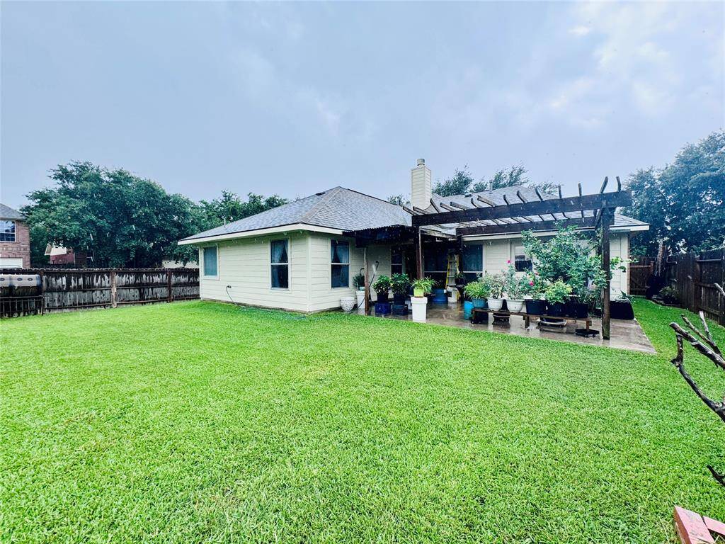 Spacious backyard featuring a well-maintained lawn, a cozy single-story house with light-colored siding, and a charming pergola adorned with potted plants. Perfect for outdoor relaxation and gardening.