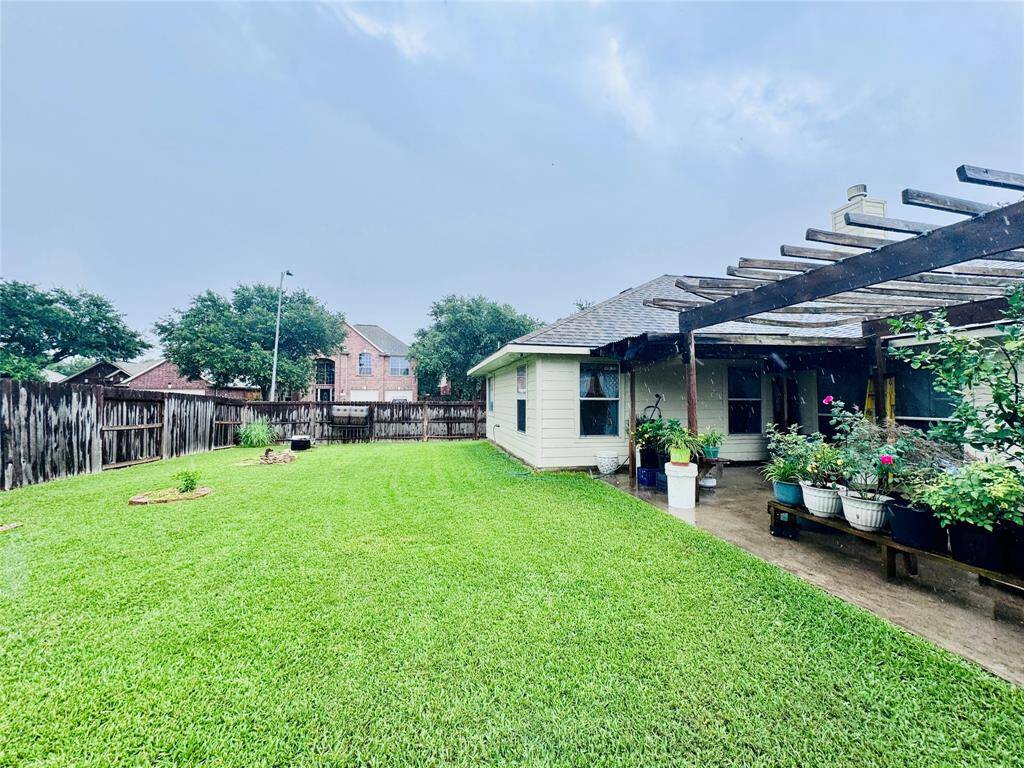 A spacious backyard featuring a well-maintained lawn and a wooden pergola. The area is bordered by a wooden fence, providing privacy. The patio adds a touch of greenery and charm to the outdoor space. Ideal for relaxation or entertaining.