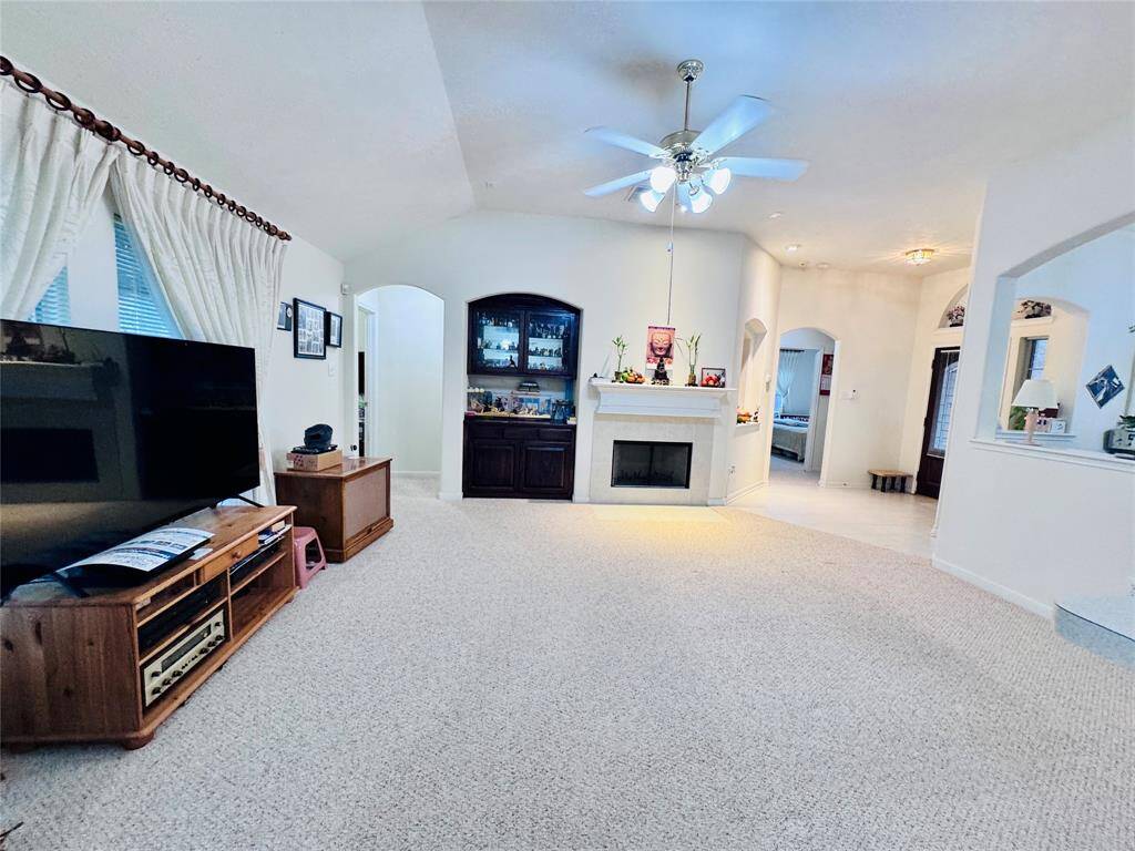 This inviting living room features a cozy fireplace, ceiling fan, and ample natural light. It offers a spacious layout with neutral carpet and easy access to adjoining rooms, perfect for relaxing or entertaining.