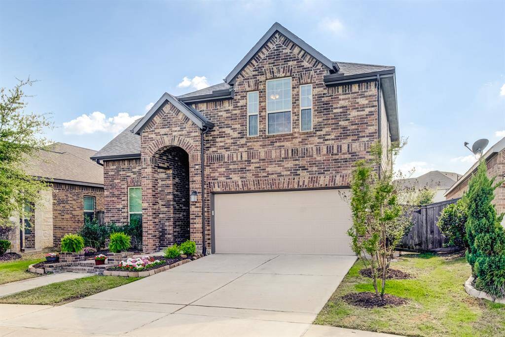 The home's facade includes a mix of brick and siding, with updated windows and a classic front door that complements the overall design. A spacious driveway leads to an attached garage, offering convenience and functionality.