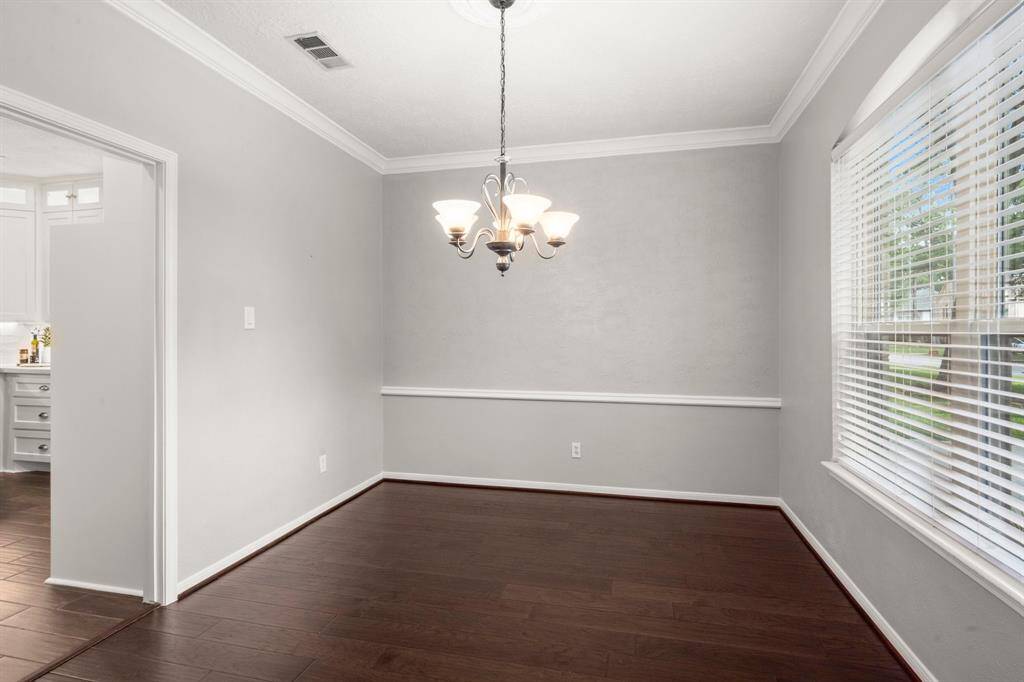 Dining room features rich wood flooring, a classic chandelier, and crisp white moldings that add timeless elegance, all with convenient direct access to the kitchen.