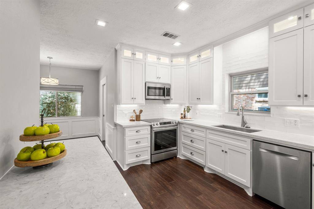 Timeless white kitchen boasts floor-to-ceiling cabinetry, under-cabinet and interior cabinet lighting, a classic subway tile backsplash, and sleek quartz countertops—combining function with elegant design.