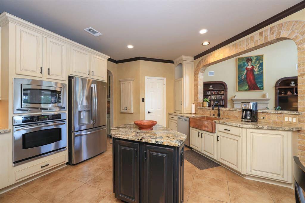 Stainless appliances, copper farm sink, side "vitamin" cabinet with puck lighting above. Custom stone arched surround. "Things to do" chalkboard with doors.