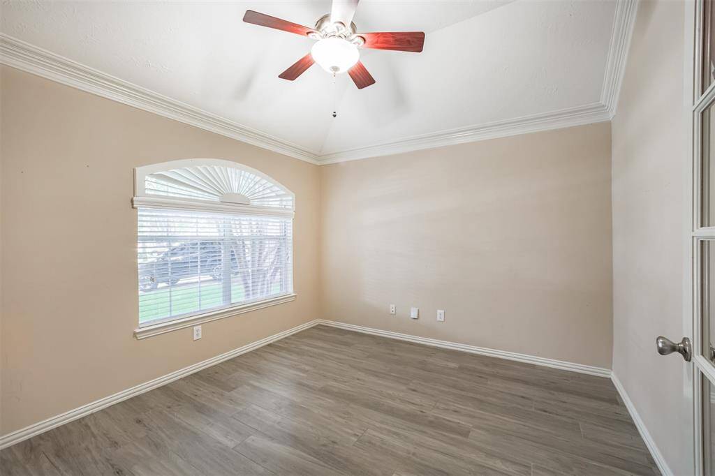 Bright and inviting home office with elegant crown molding, a ceiling fan, and abundant natural light from a charming arched window.