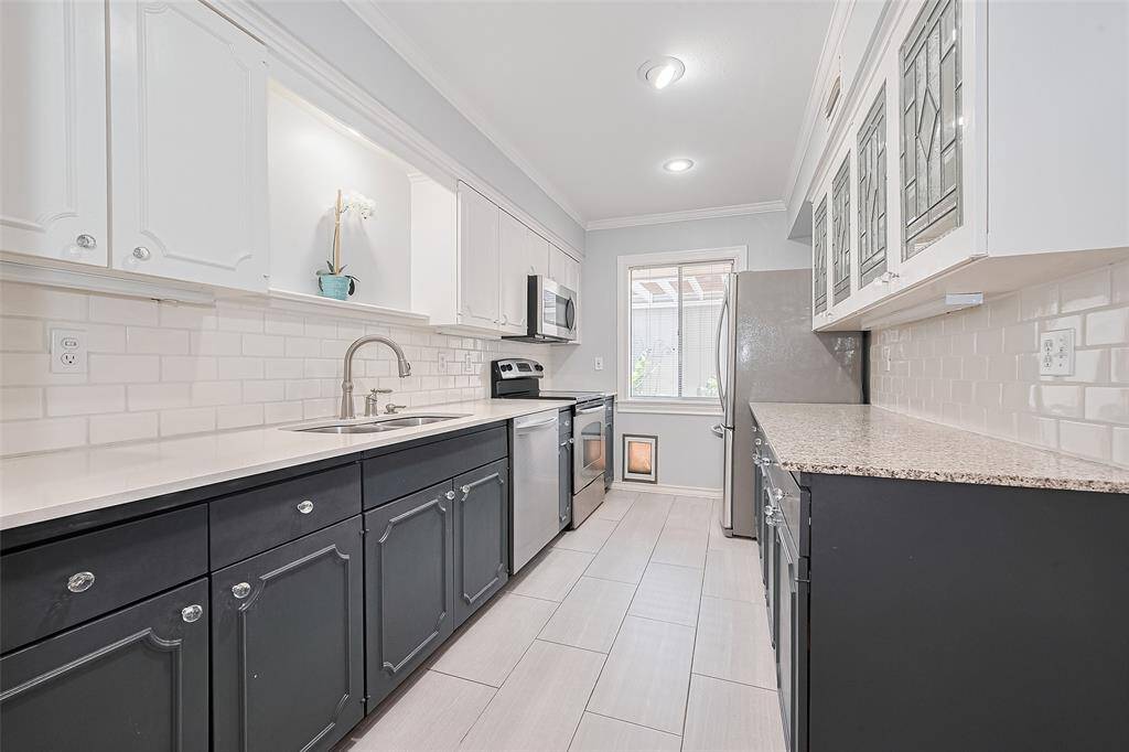 This thoughtfully updated kitchen blends modern convenience with classic charm. Two-tone cabinetry, featuring white uppers and deep navy lowers, accented by glass hardware and designer molding. A subway tile backsplash, solid-surface countertops, and stainless steel appliances give the space a clean, contemporary feel.