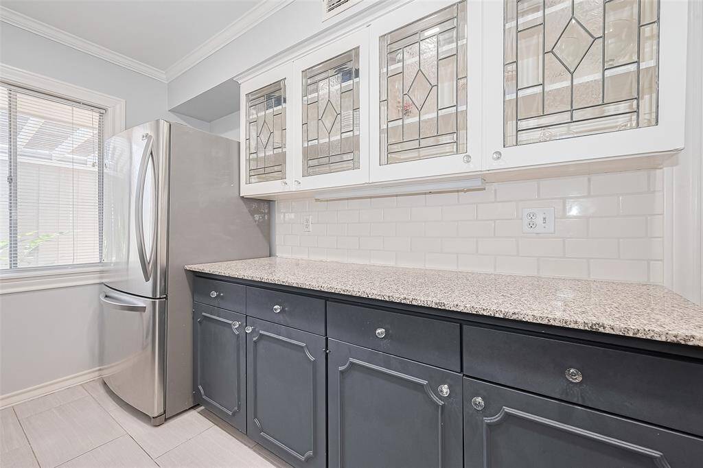 Enjoy ample prep space, a deep undermount sink with brushed nickel fixtures, and a stunning built-in glass cabinet with leaded detailing—perfect for displaying serve ware or collectibles. With abundant storage, a window overlooking the patio, and sleek tile flooring, this kitchen is both functional and full of character.